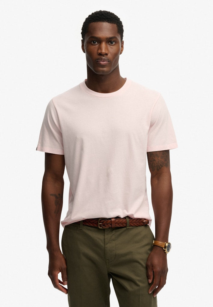 Man wearing a light pink t-shirt and green pants on a white background