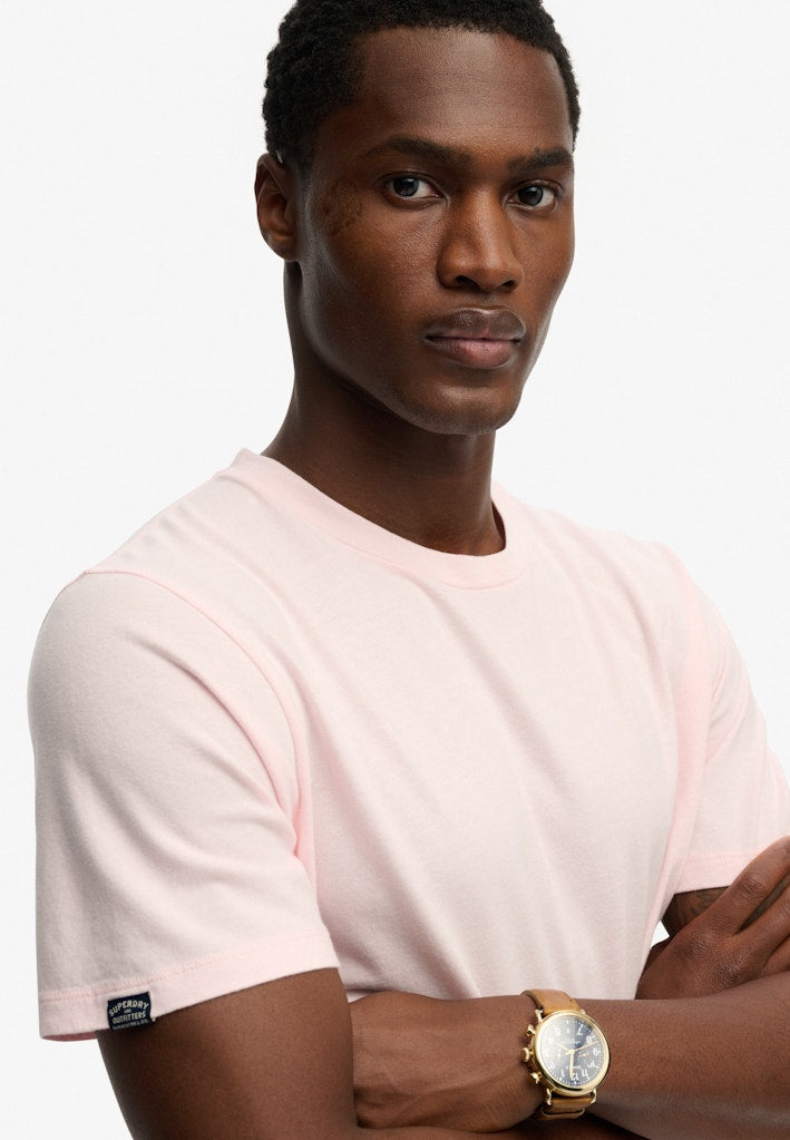Man wearing a light pink t-shirt with a gold watch on a white background
