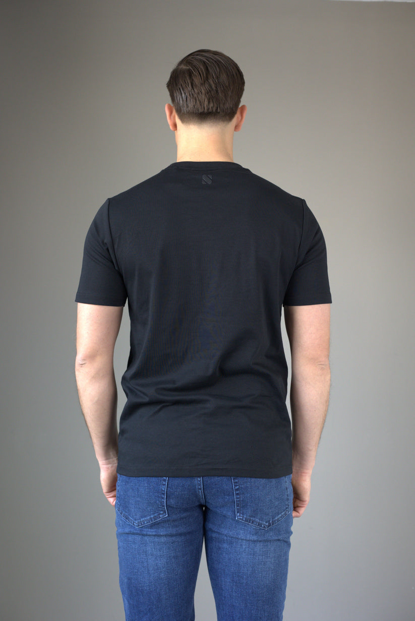 Person wearing a black t-shirt and blue jeans against a gray background