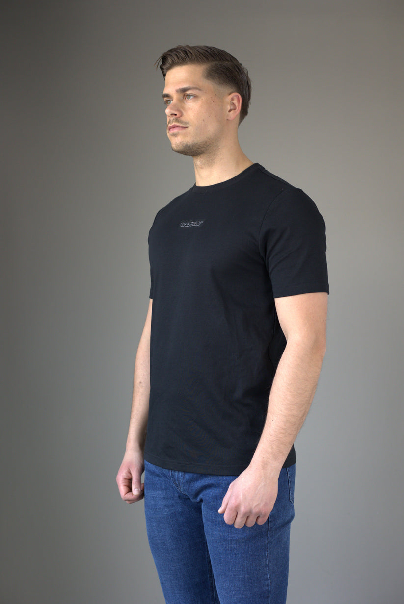 Man wearing a black t-shirt and blue jeans against a gray background