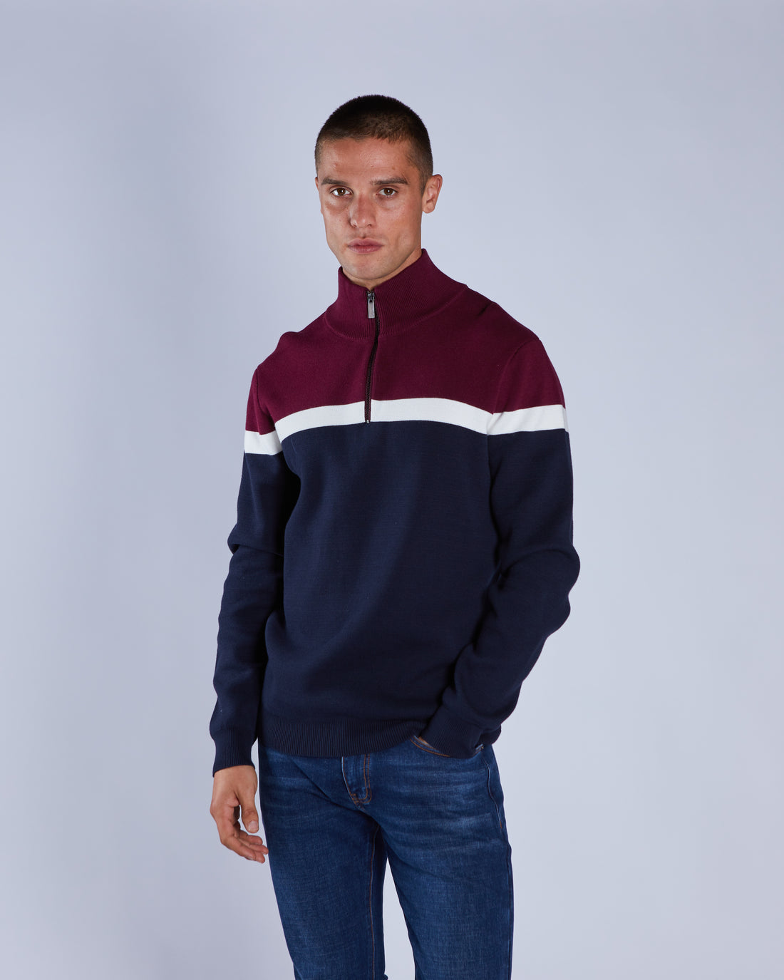Man wearing a maroon and navy half-zip sweatshirt with a white stripe on a gray background