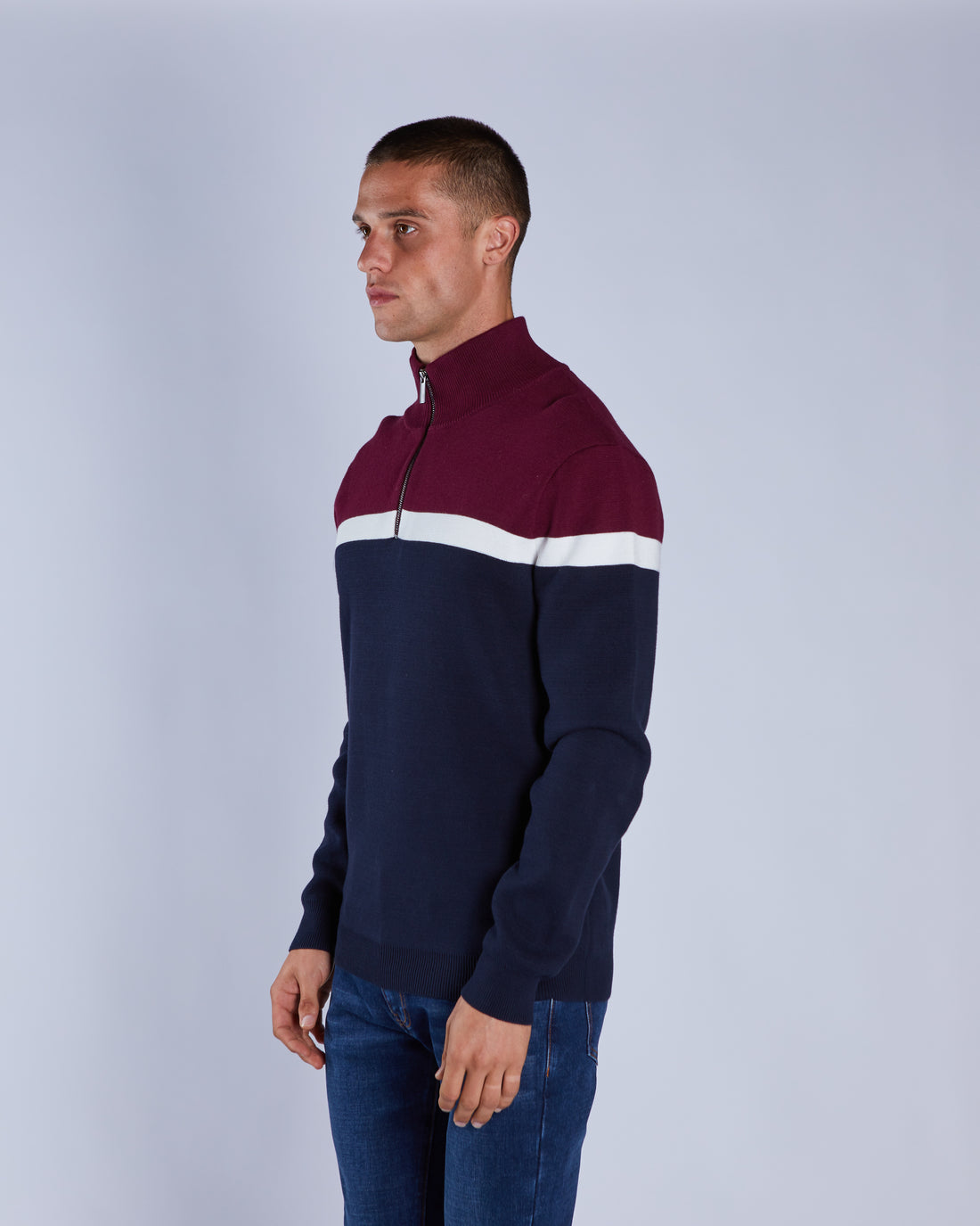 Man wearing a two-tone sweater with maroon and navy sections on a light gray background