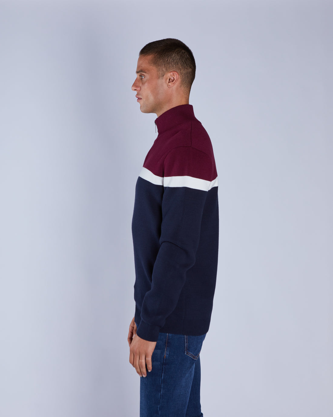 Man wearing a two-tone sweater with maroon and navy sections on a plain background