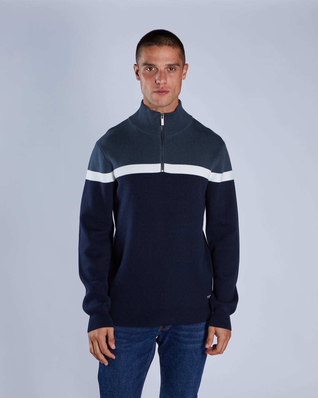 Man wearing a navy blue sweater with a white stripe on a light gray background