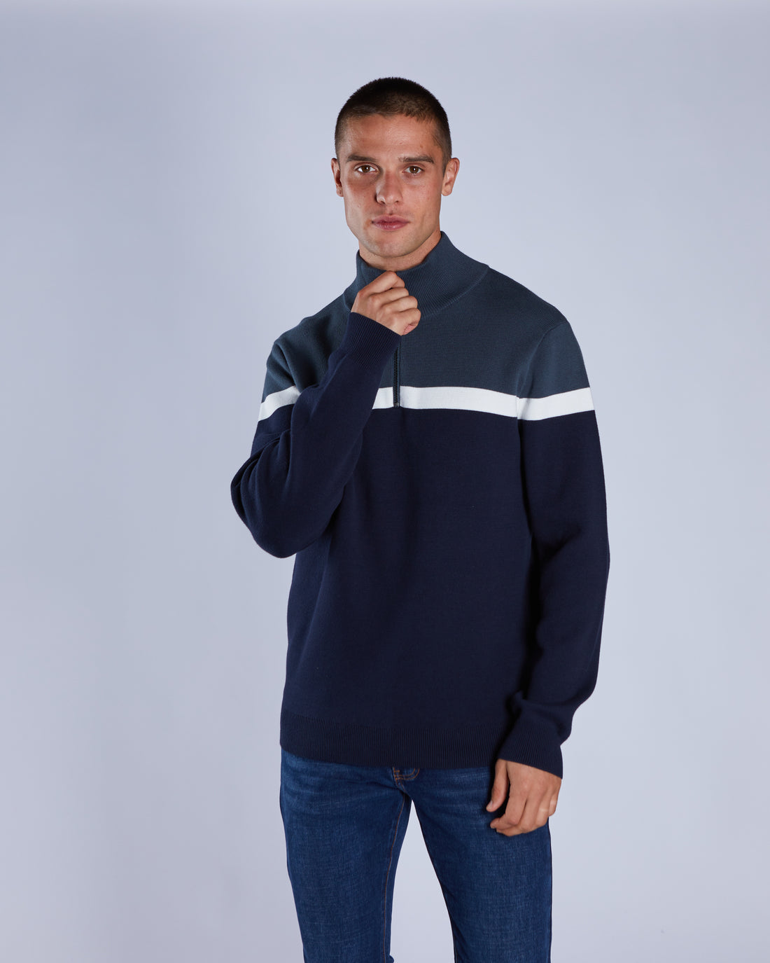 Man wearing a navy sweater with a white stripe on a light gray background