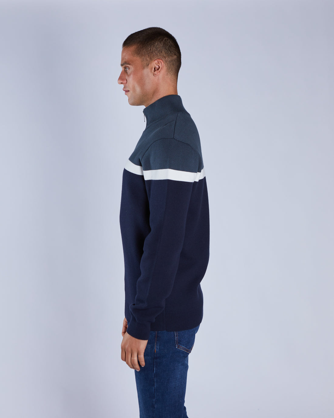 Man wearing a navy sweater with a white stripe on a light gray background