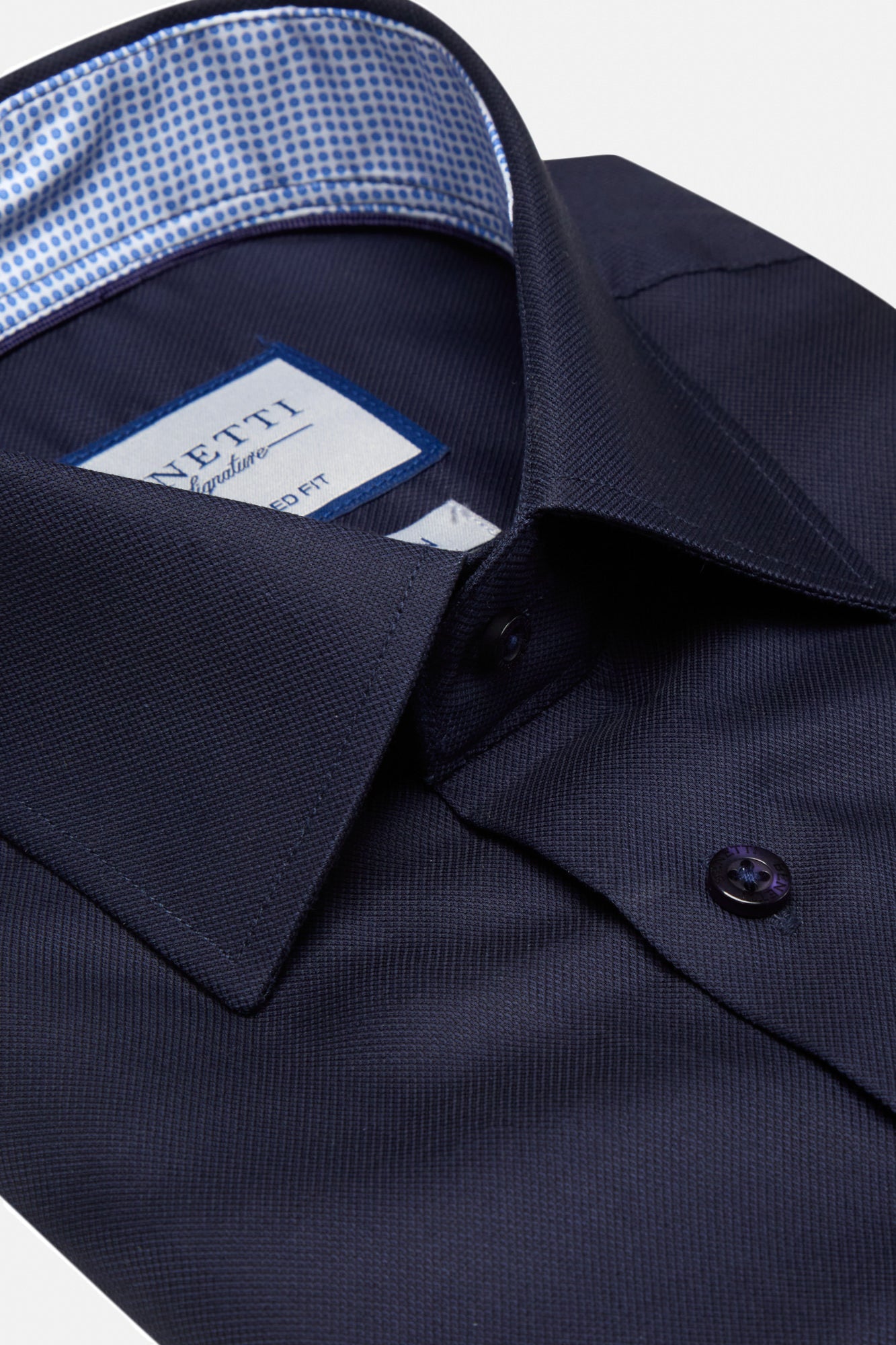 Close-up of a navy blue dress shirt with a Vetti label on a white background