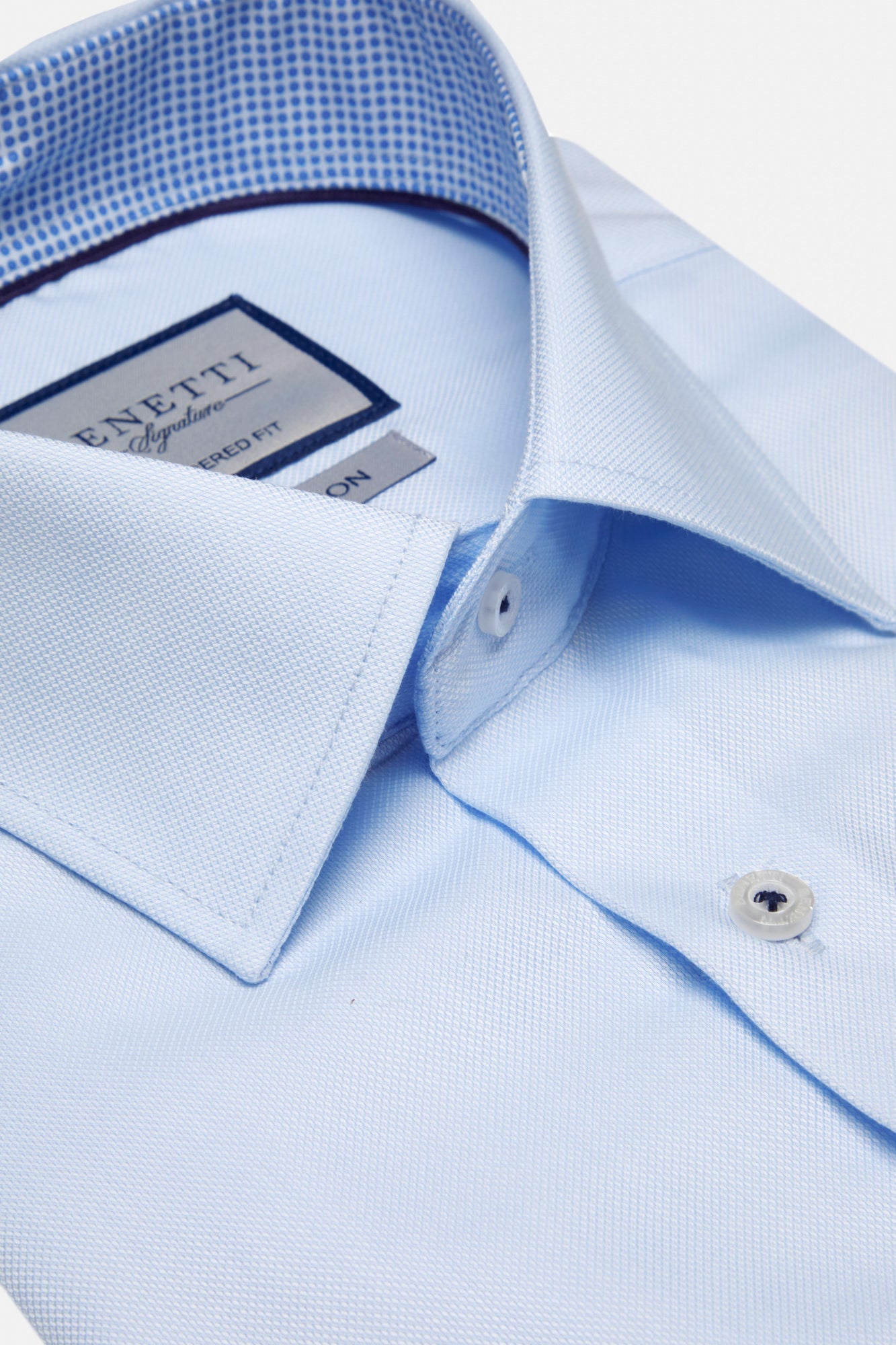 Close-up of a light blue dress shirt with a brand label on a white background