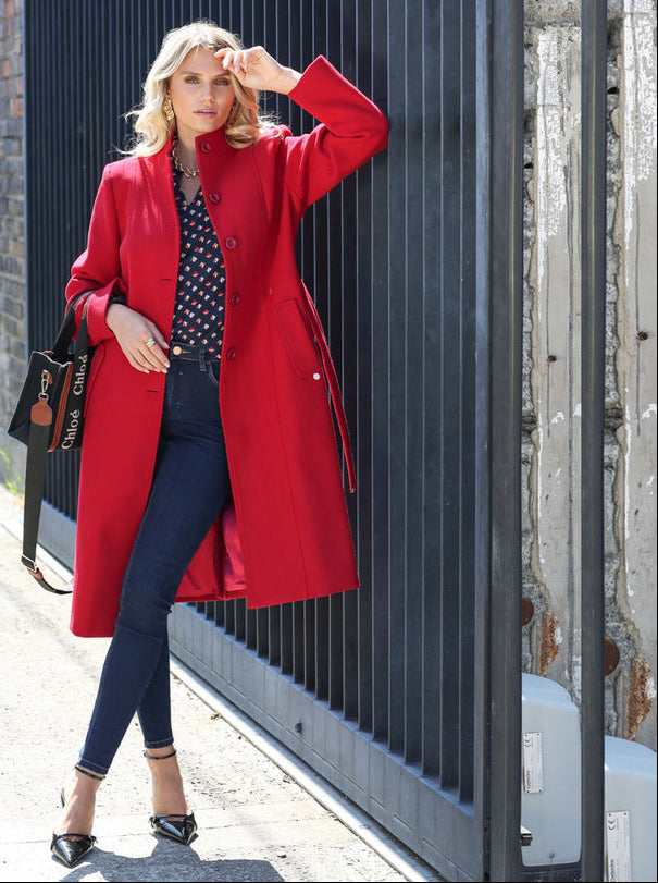 Woman wearing a red coat standing against a black metal gate.