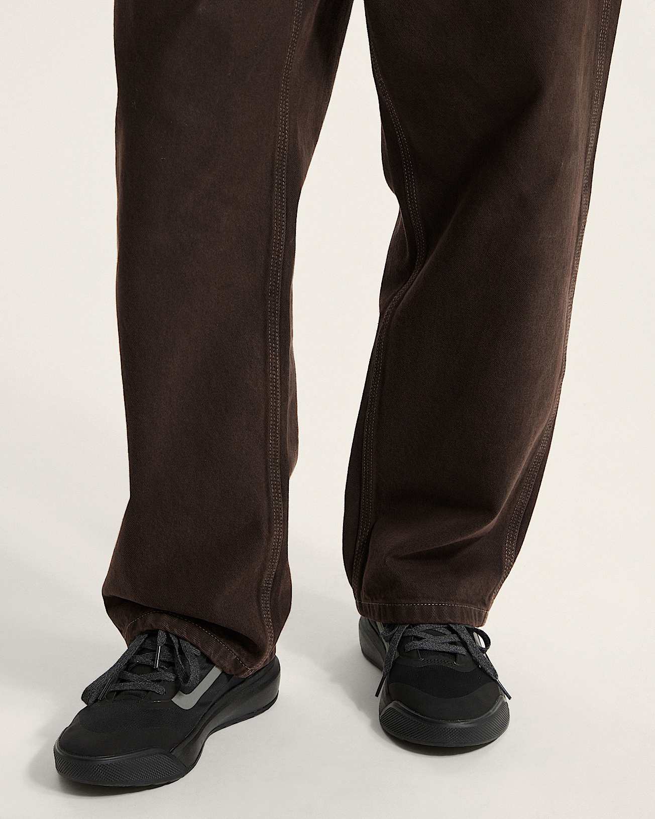 Brown pants and black sneakers worn by a person on a plain background