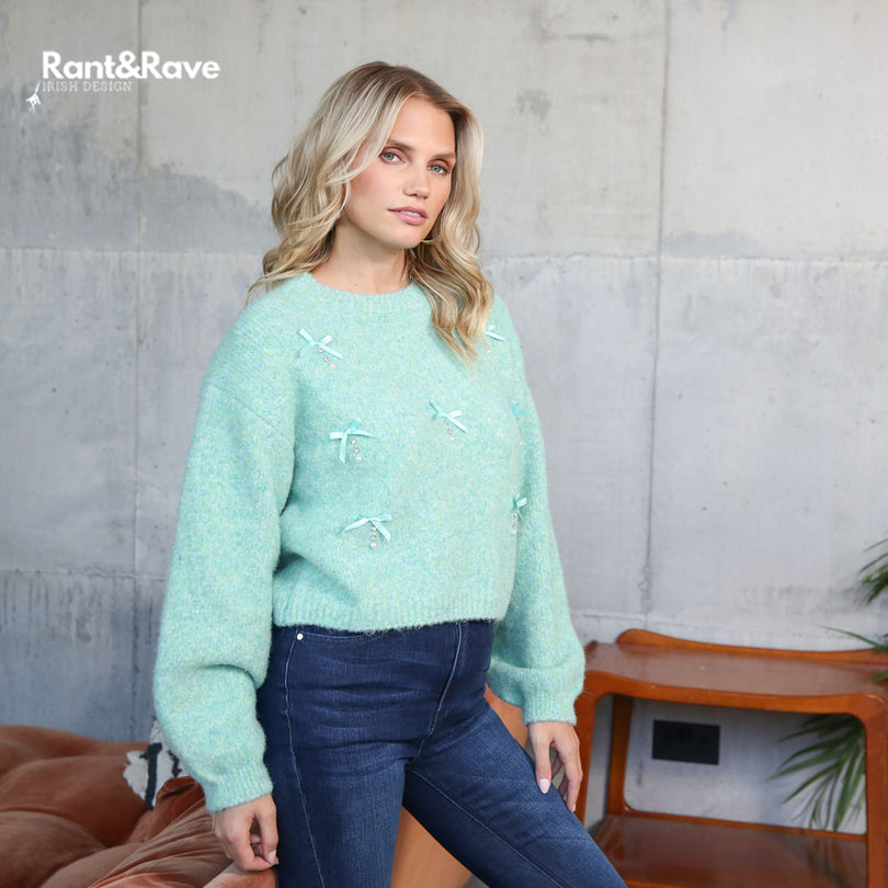 Woman wearing a light green sweater with white patterns against a gray wall.