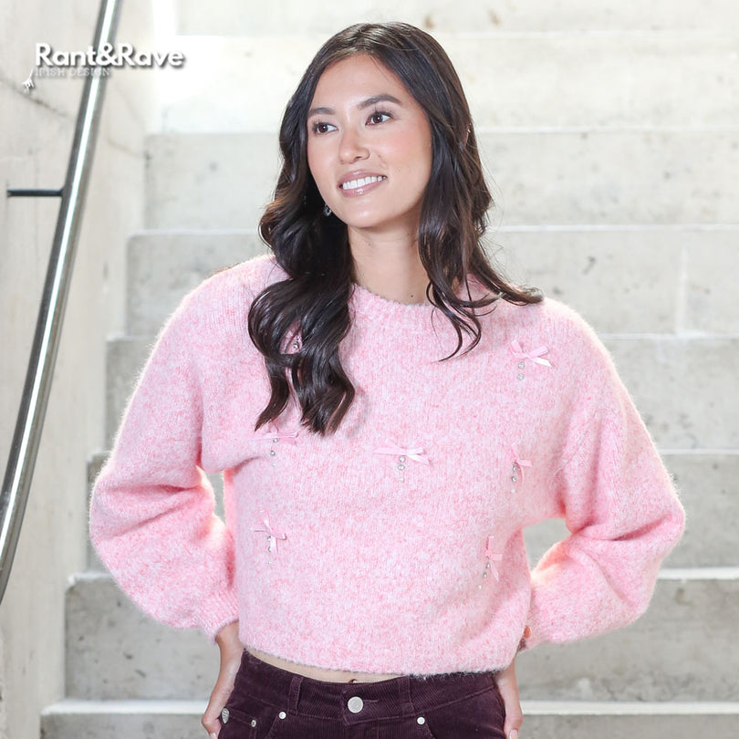 Woman wearing a pink sweater standing on stairs with 'Rant&Rave' logo.