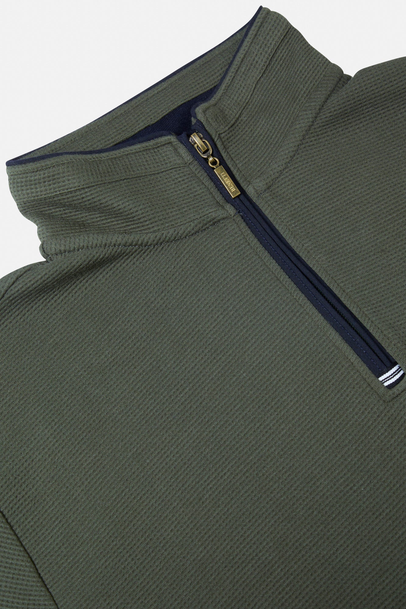 Close-up of a green zip-up sweatshirt with a brand logo on a light gray background