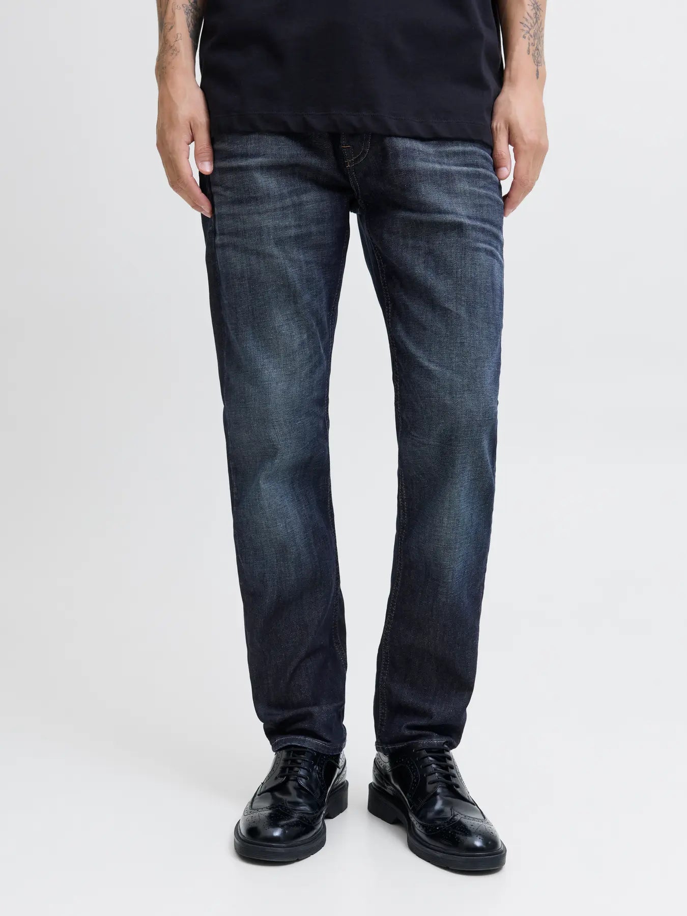 Person wearing dark blue jeans and black shoes on a white background