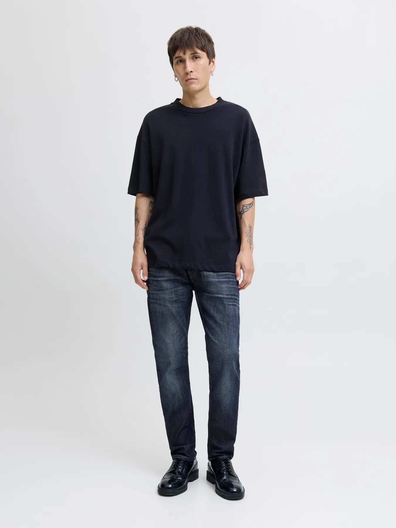 Person wearing a black oversized t-shirt and dark jeans on a white background