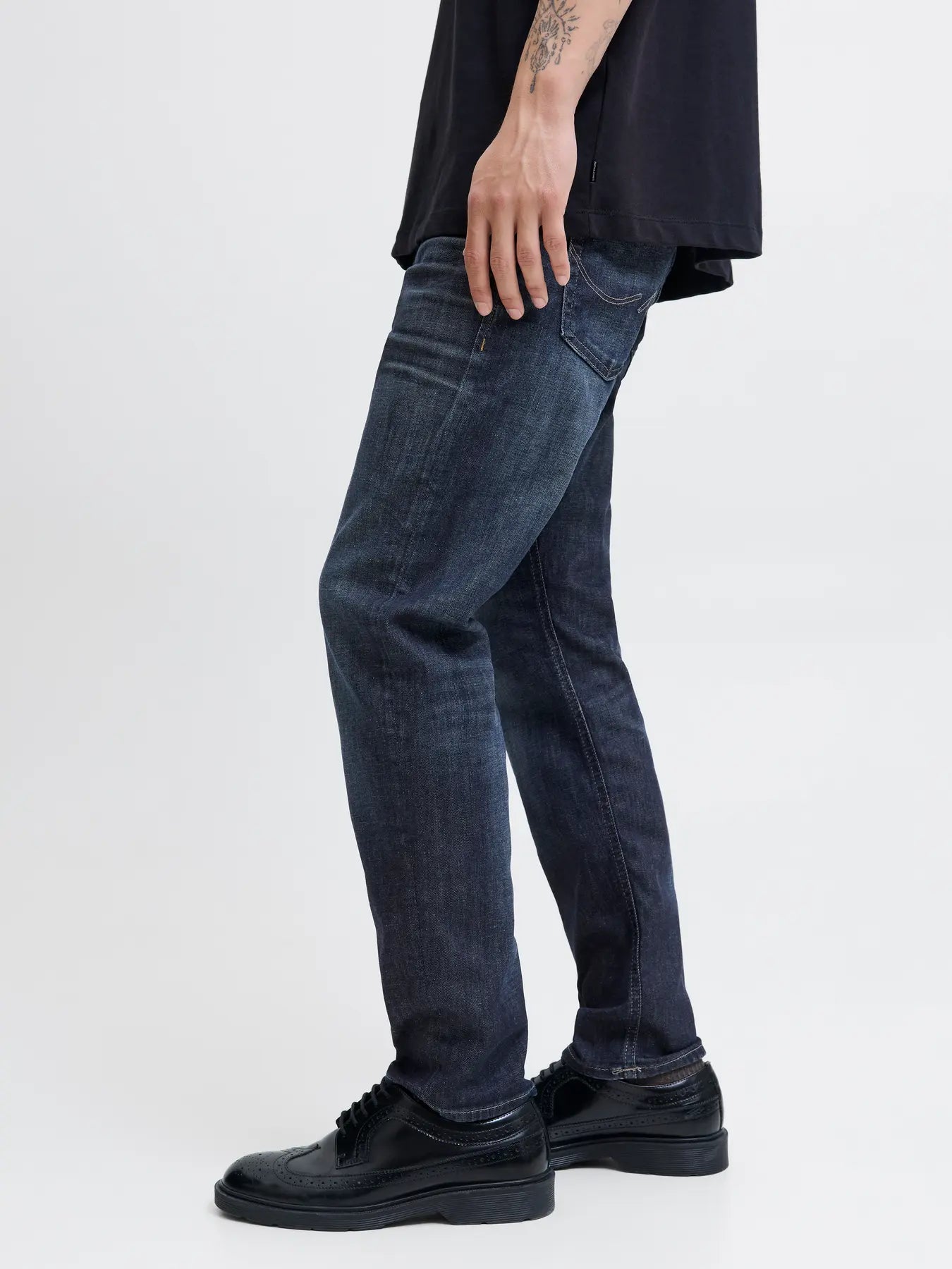 Person wearing dark blue jeans and black shoes on a white background