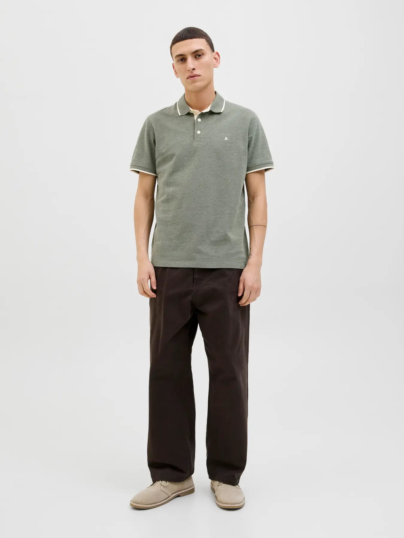 Man wearing a green polo shirt and dark pants on a white background