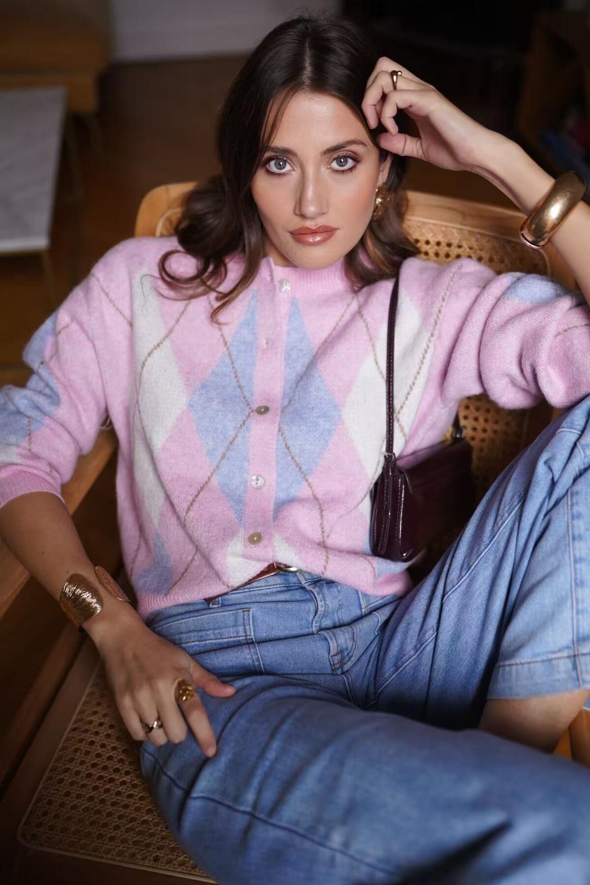Woman wearing a pink cardigan and blue jeans sitting on a chair.