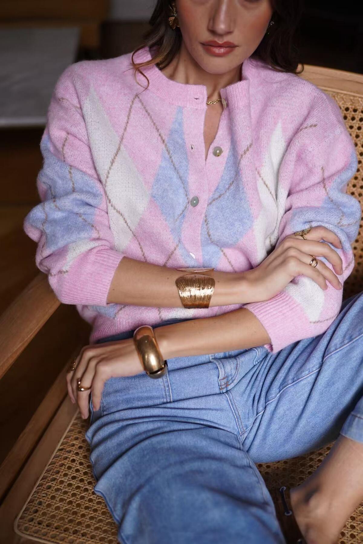 Person wearing a pastel sweater and blue jeans sitting on a wicker chair.