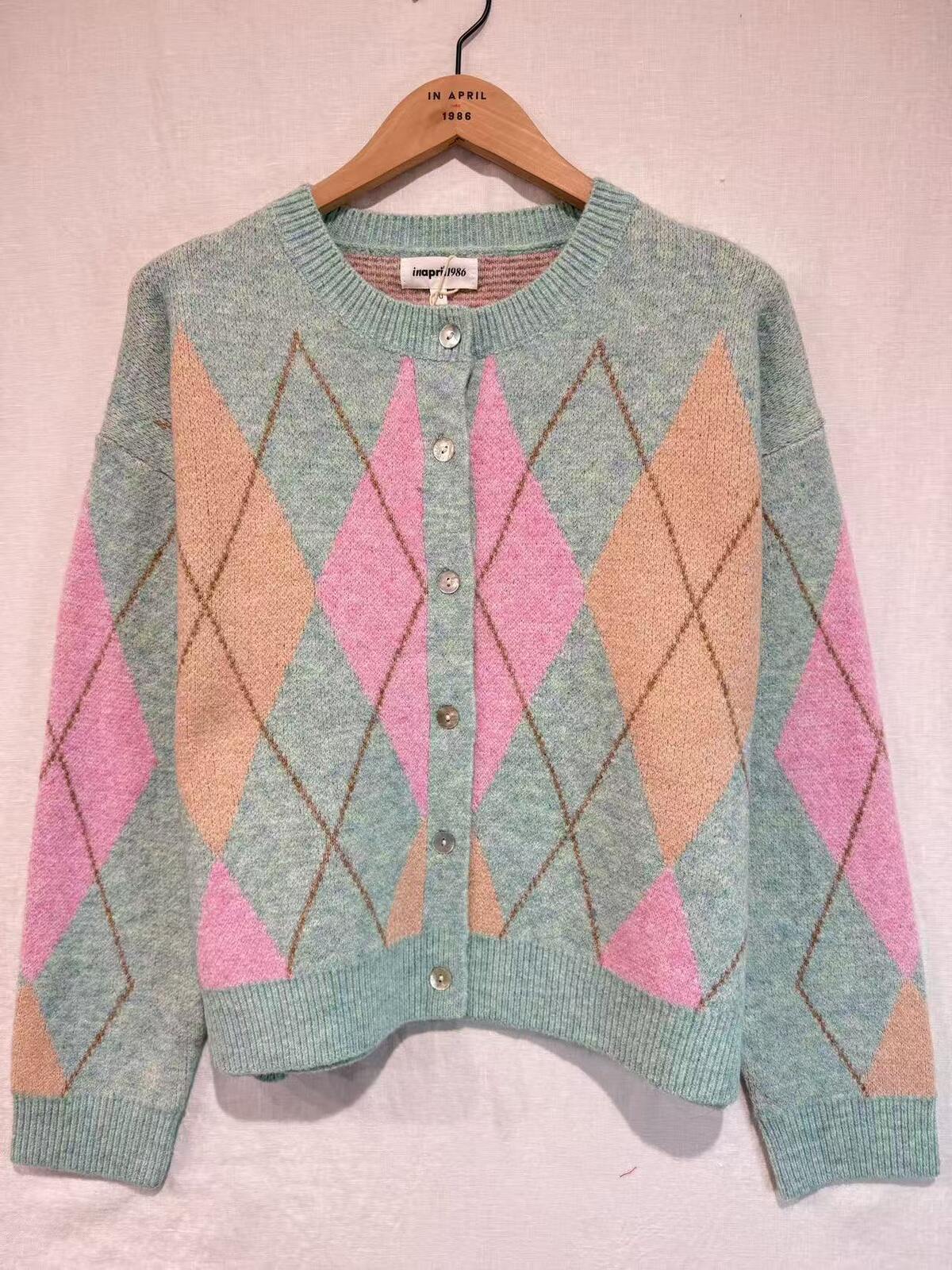 Knitted sweater with pink and beige diamond pattern on a hanger against a light pink background