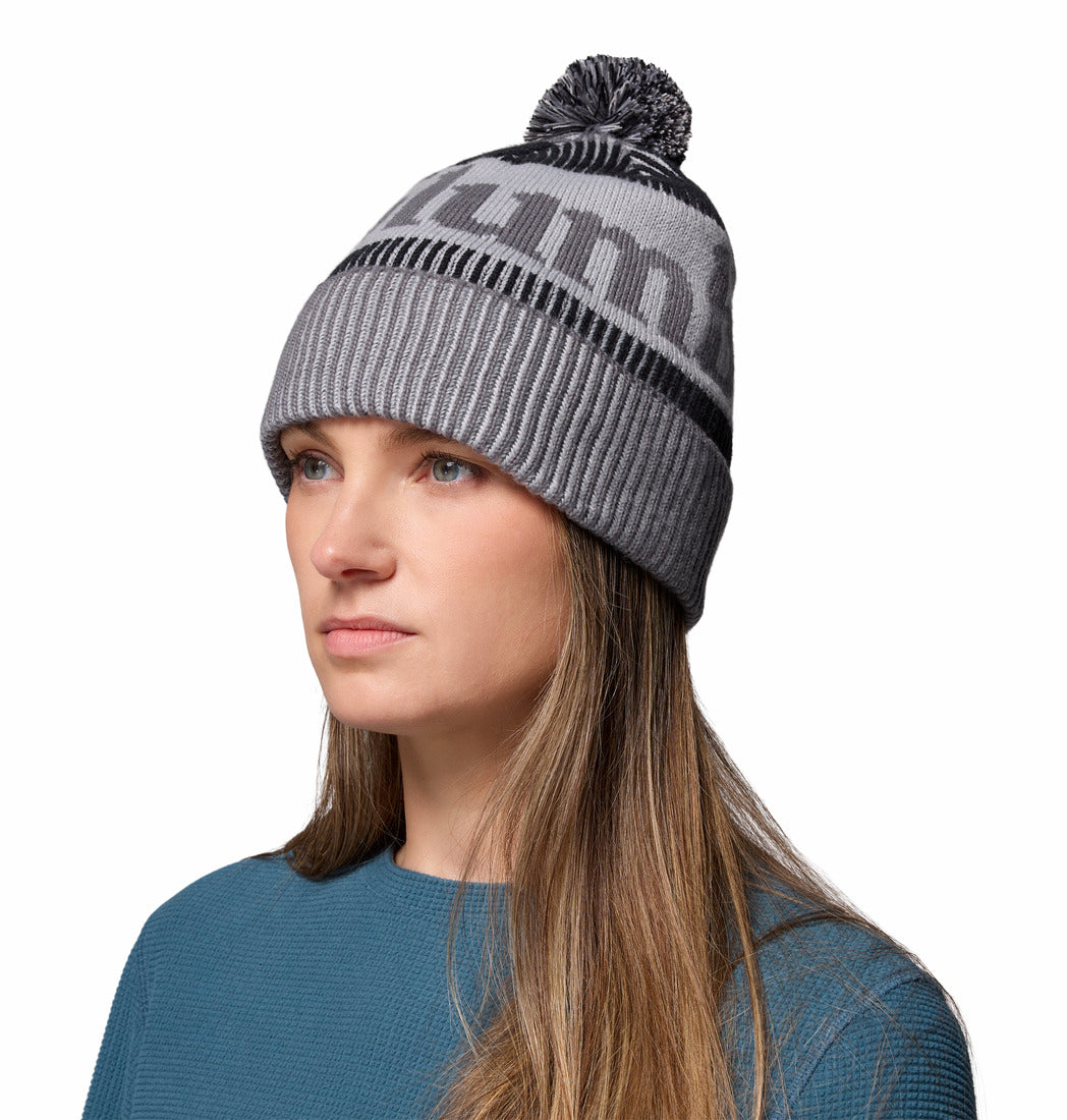 Woman wearing a gray knit beanie with a brand logo on a white background