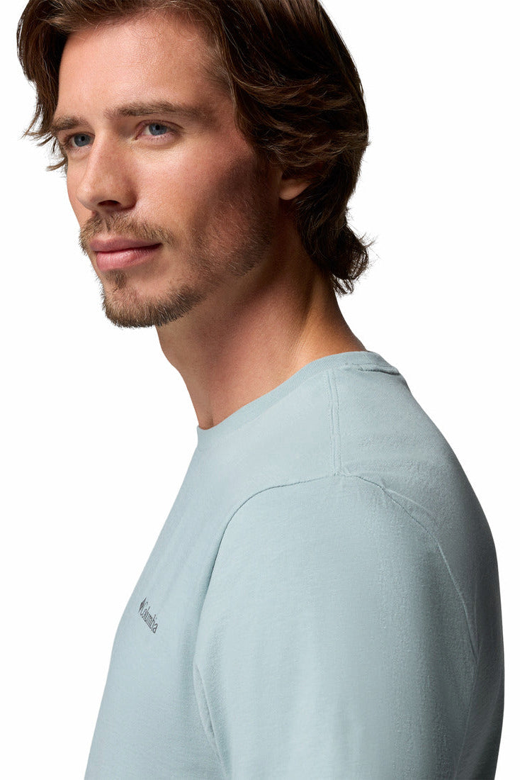 Man wearing a light blue t-shirt with a brand logo on a white background