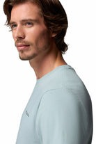 Man wearing a light blue t-shirt with a brand logo on a white background