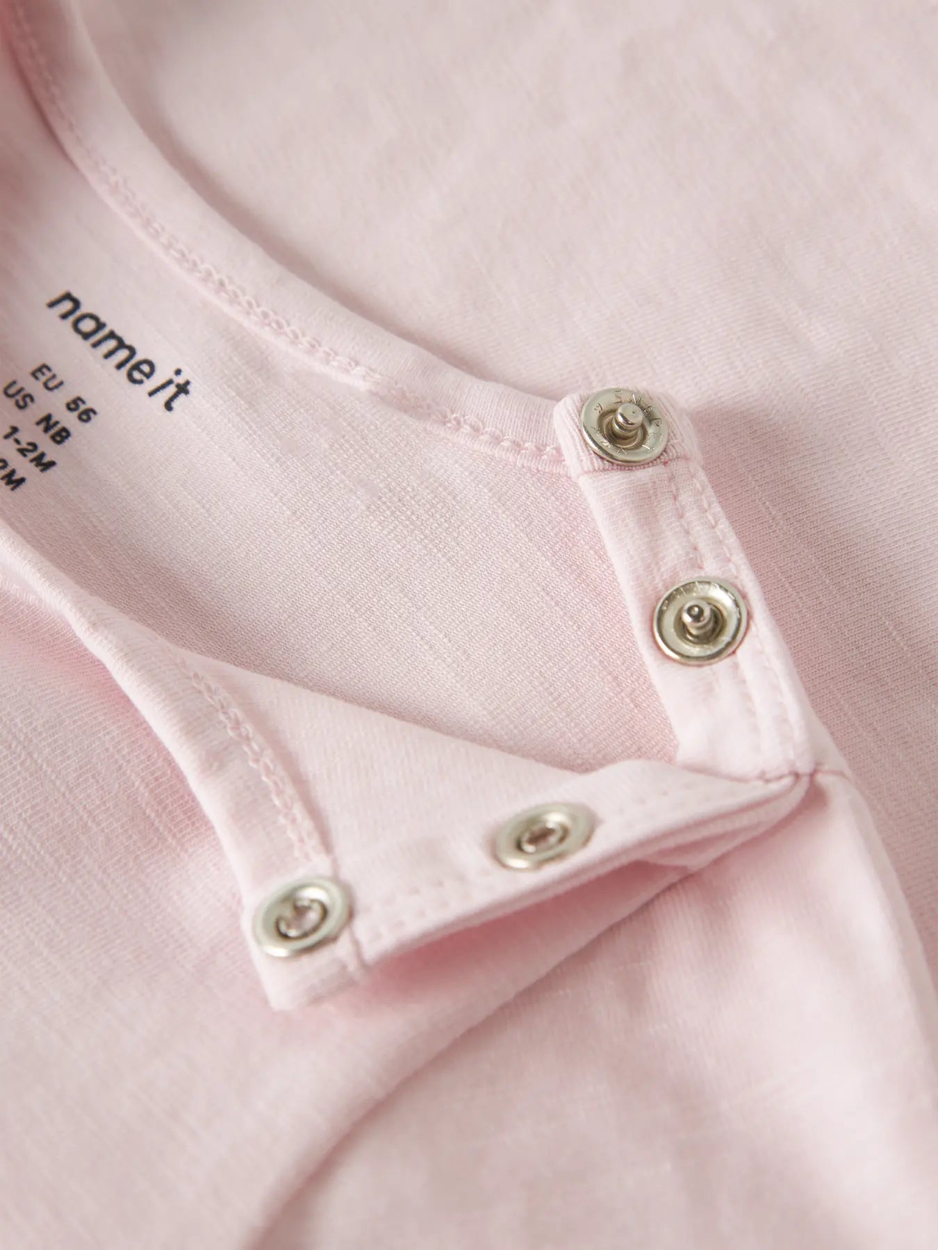 Close-up of a pink garment with button details and 'name it' branding.