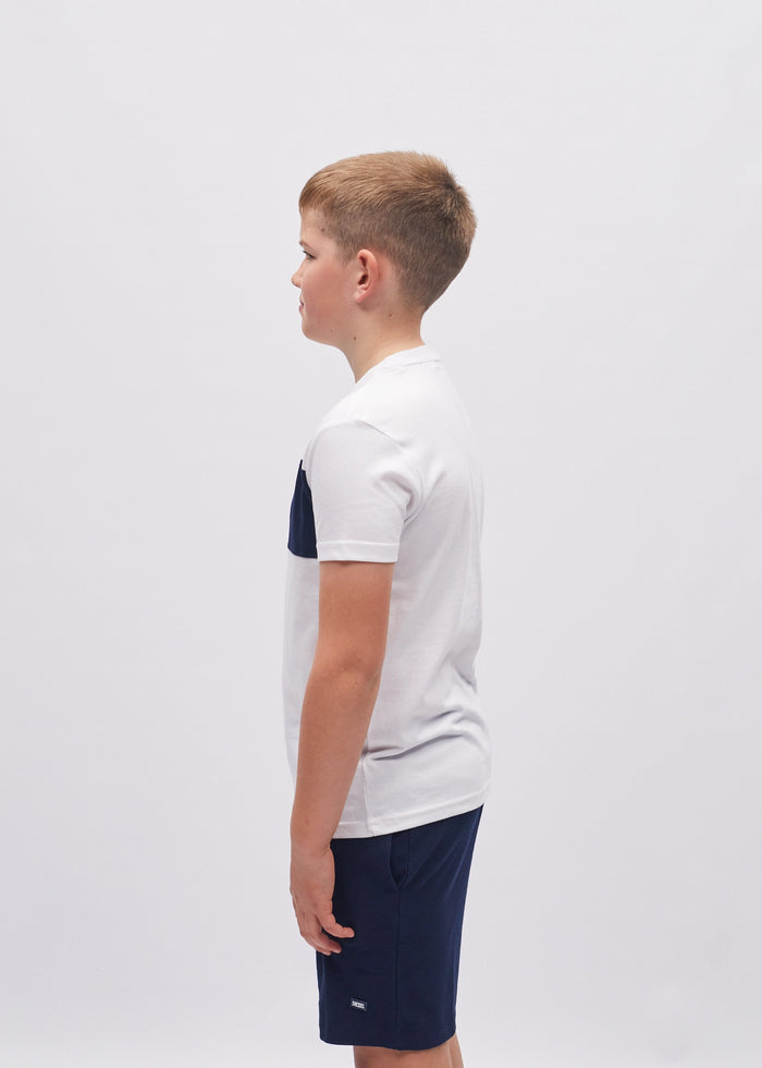 Young boy wearing a white t-shirt with a navy logo and dark shorts on a light gray background