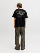 Person wearing a black 'Originals Studio' t-shirt on a white background