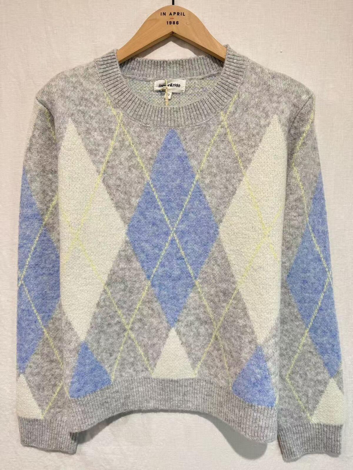 Gray sweater with blue and white diamond pattern on a wooden hanger against a beige wall.