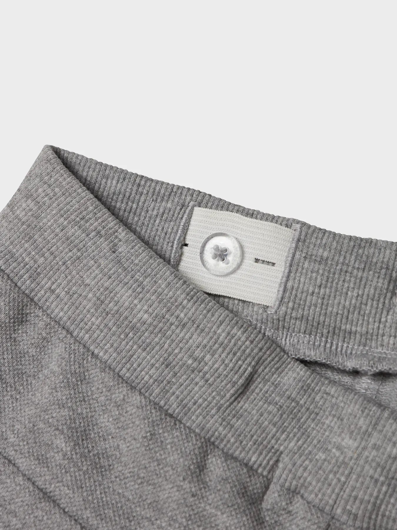 Close-up of a gray fabric waistband with a brand label on a light gray background