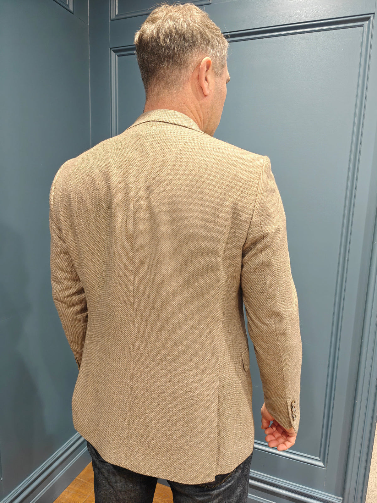 Man wearing a beige blazer against a gray wall