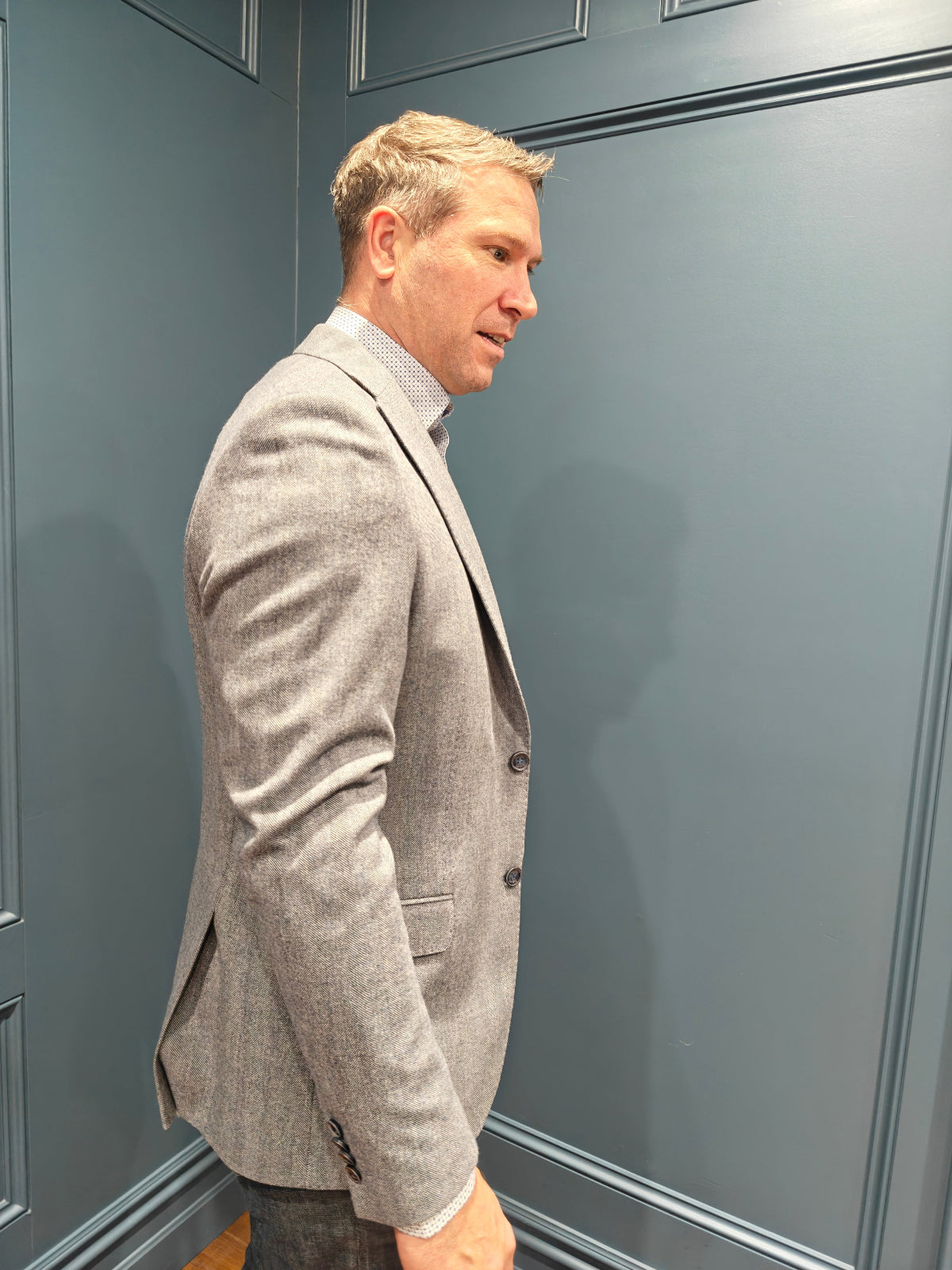 Man wearing a gray blazer standing against a gray wall.