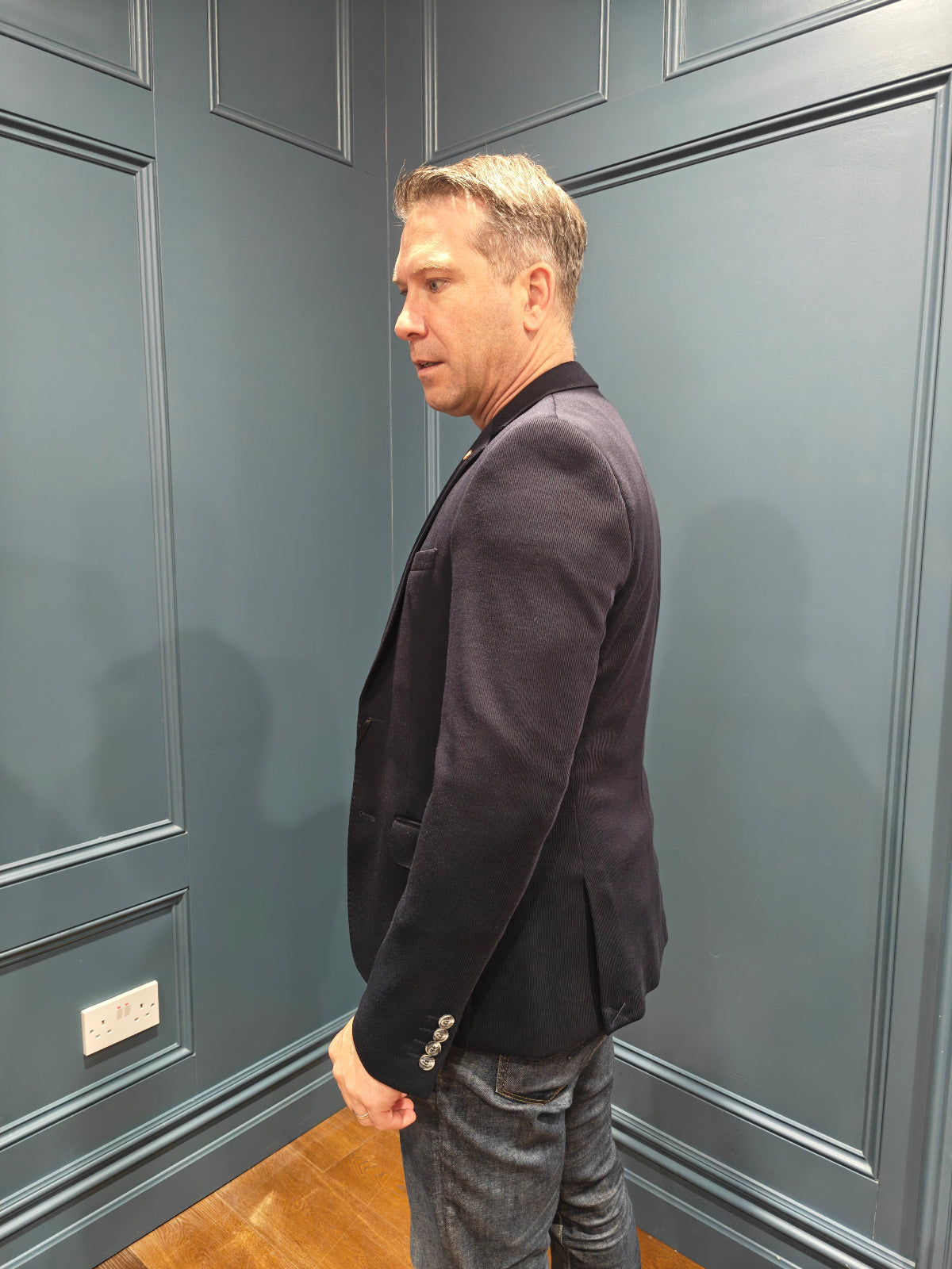 Man standing against a gray paneled wall in a navy blazer