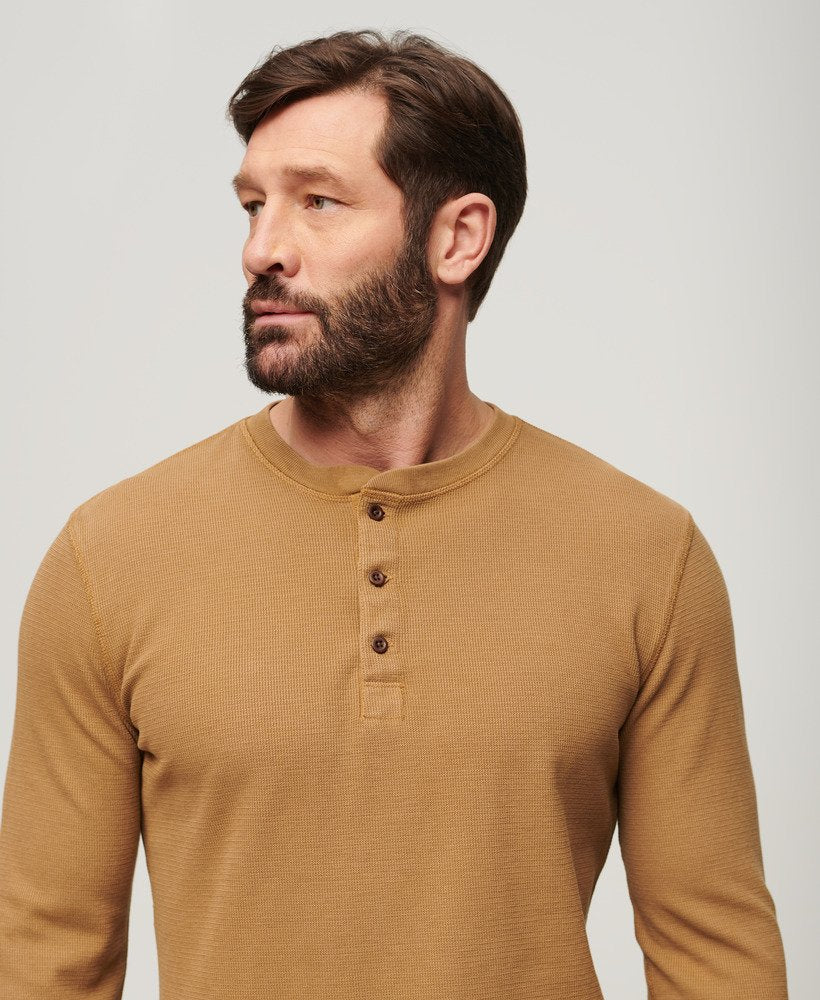 Man wearing a mustard yellow long-sleeve henley shirt against a plain background