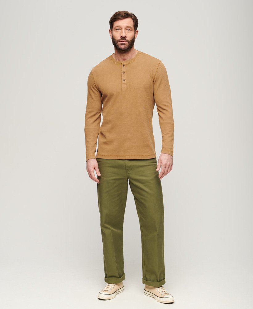Man wearing a brown long-sleeve shirt and green pants on a white background