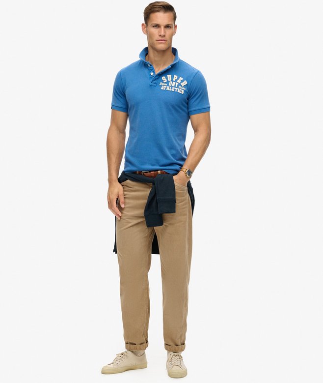 Man wearing a blue polo shirt with text and beige pants on a white background