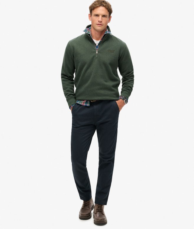 Man wearing a green pullover with a logo, navy pants, and brown boots on a white background