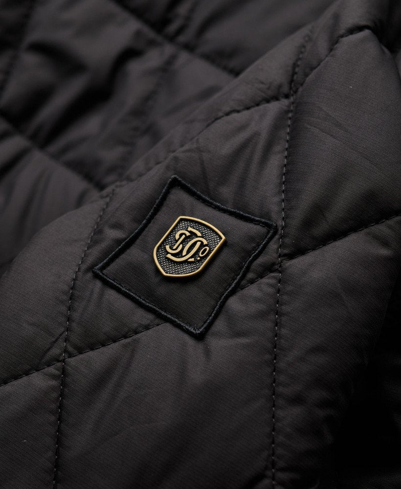 Close-up of a black quilted jacket with a gold emblem on a dark background