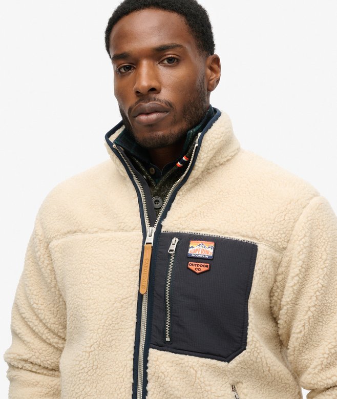 Man wearing a beige fleece jacket with a brand logo on a white background