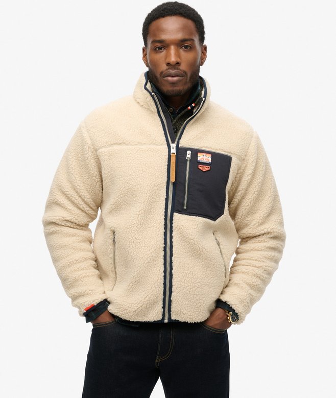 Man wearing a cream sherpa jacket with a brand logo on a white background