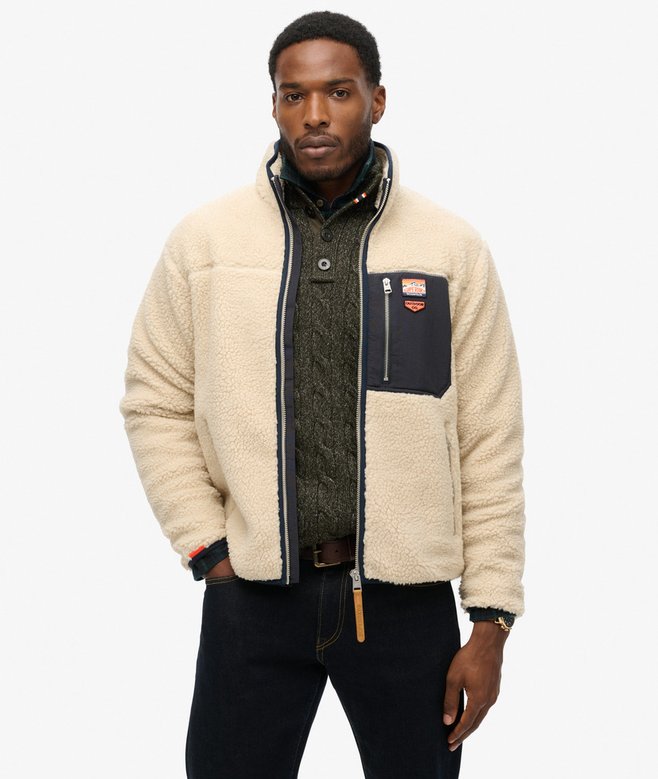 Man wearing a cream sherpa jacket with a brand logo on a white background