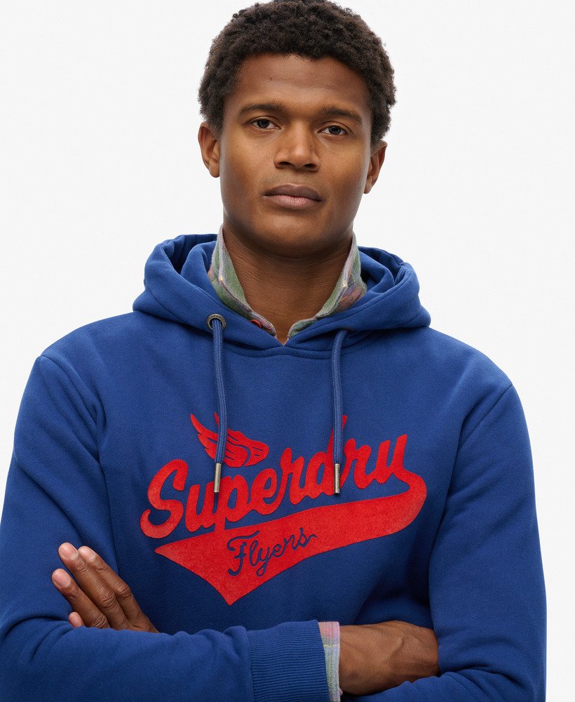Man wearing a navy blue hoodie with a Superdry flyers script longo on the front, close up view