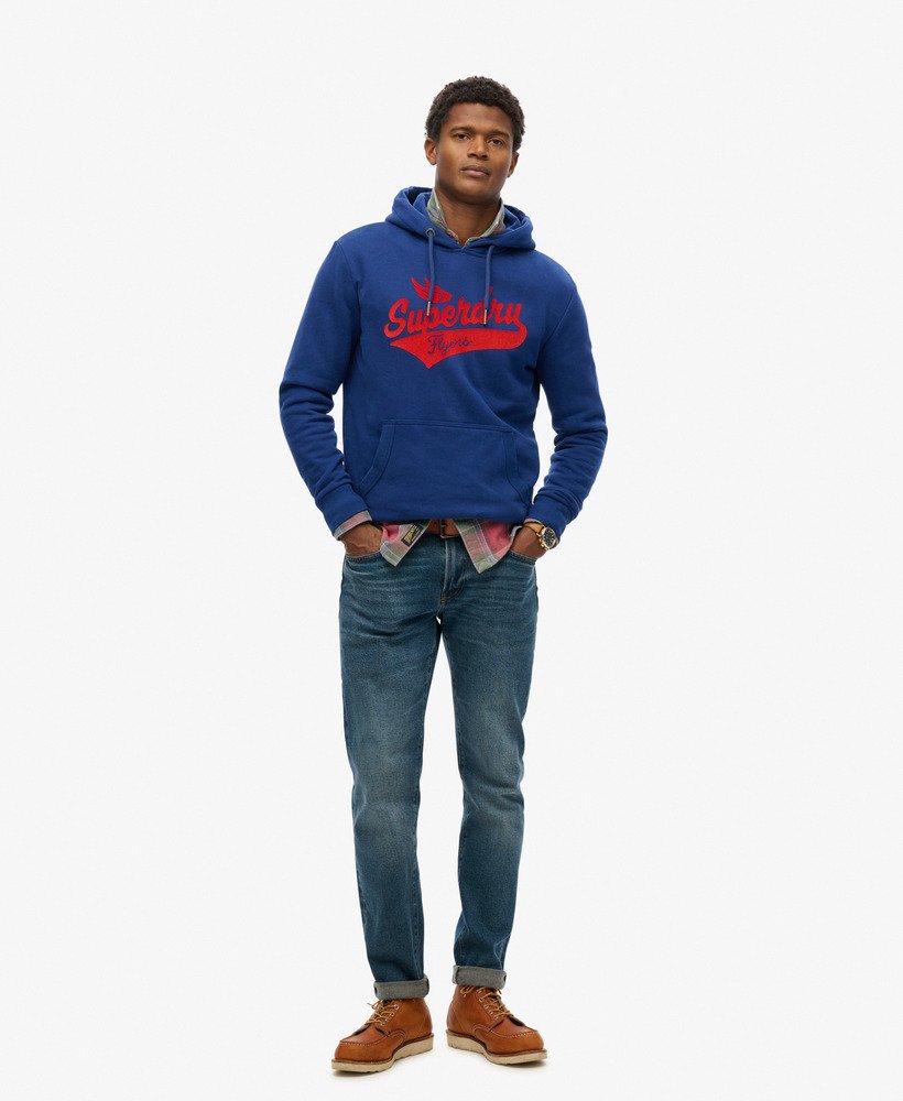 Man wearing a navy blue hoodie with a Superdry flyers script longo on the front with a pair of blue jeans and brown boots