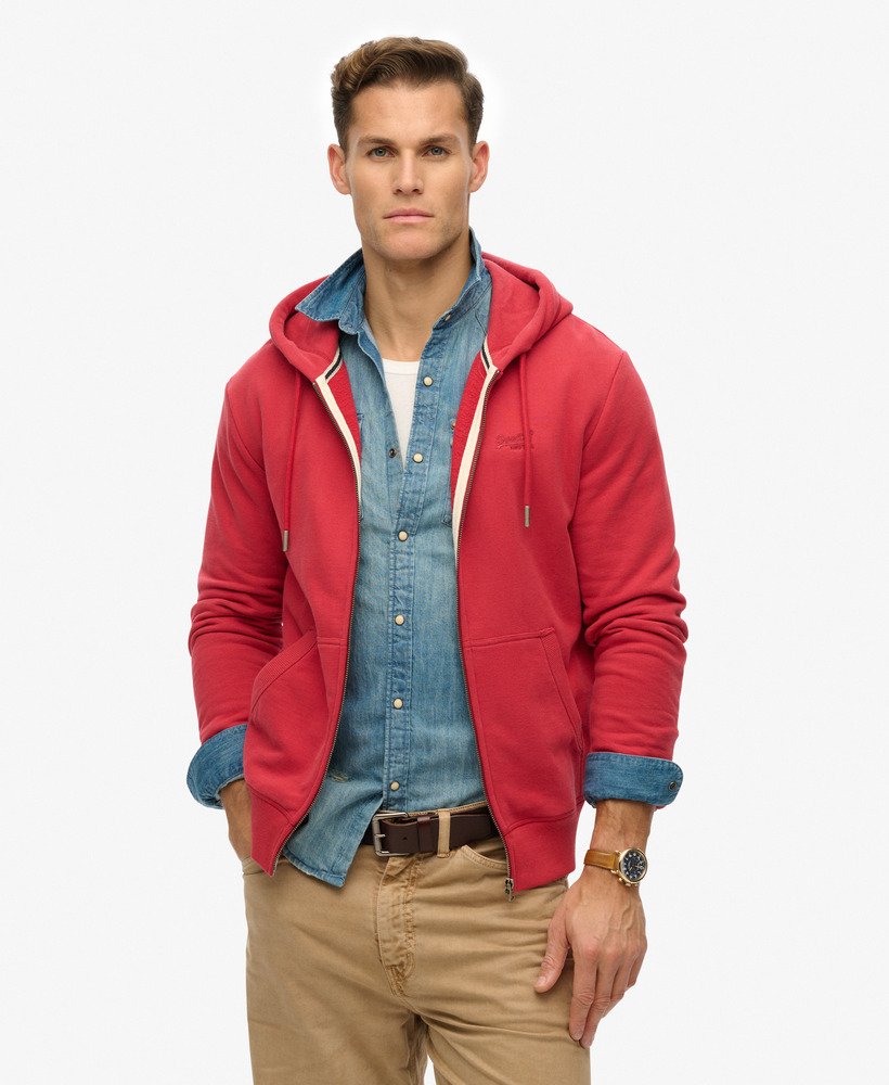 Man wearing a red hoodie over a denim shirt with beige pants on a white background