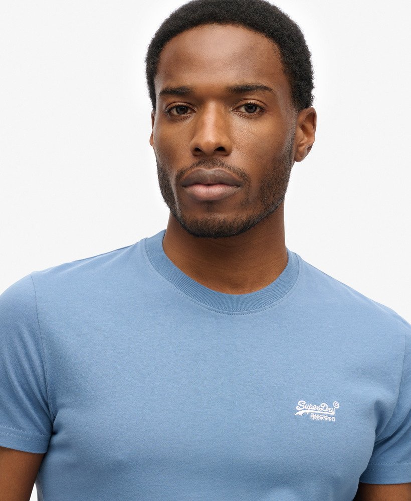 Man wearing a light blue t-shirt with a superdry logo on a white background