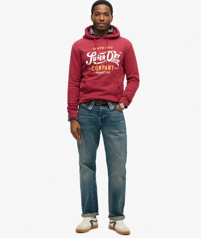 Man wearing a red hoodie with text and blue jeans on a white background