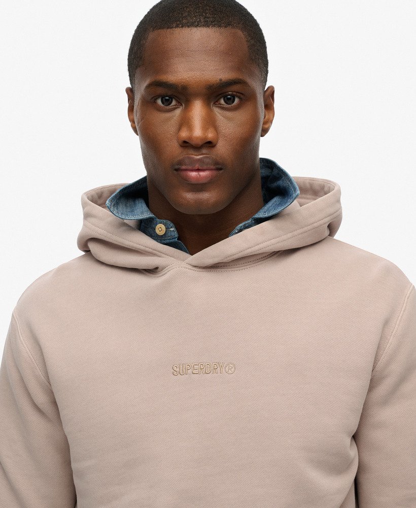 Man wearing a beige hoodie with 'Superdry' branding on a light gray background