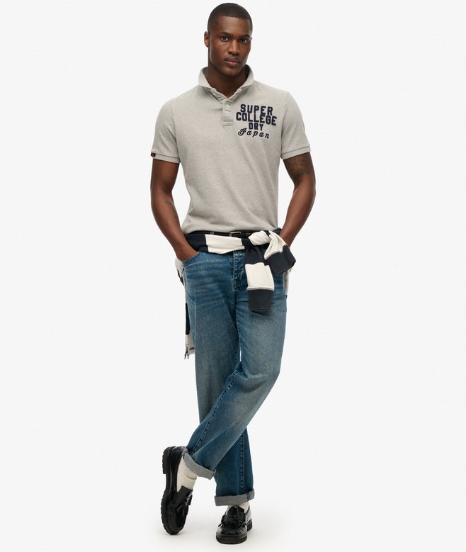 Man wearing a gray polo shirt with text and blue jeans on a white background